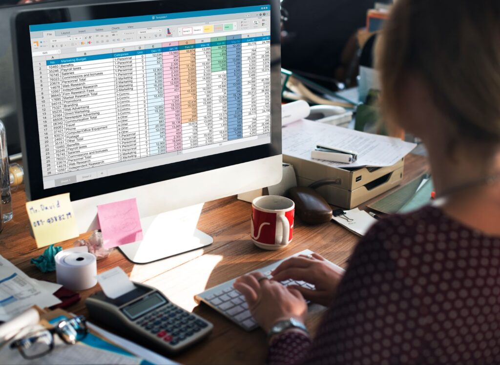 a woman typing in front of a PC screen on a messy table in the office