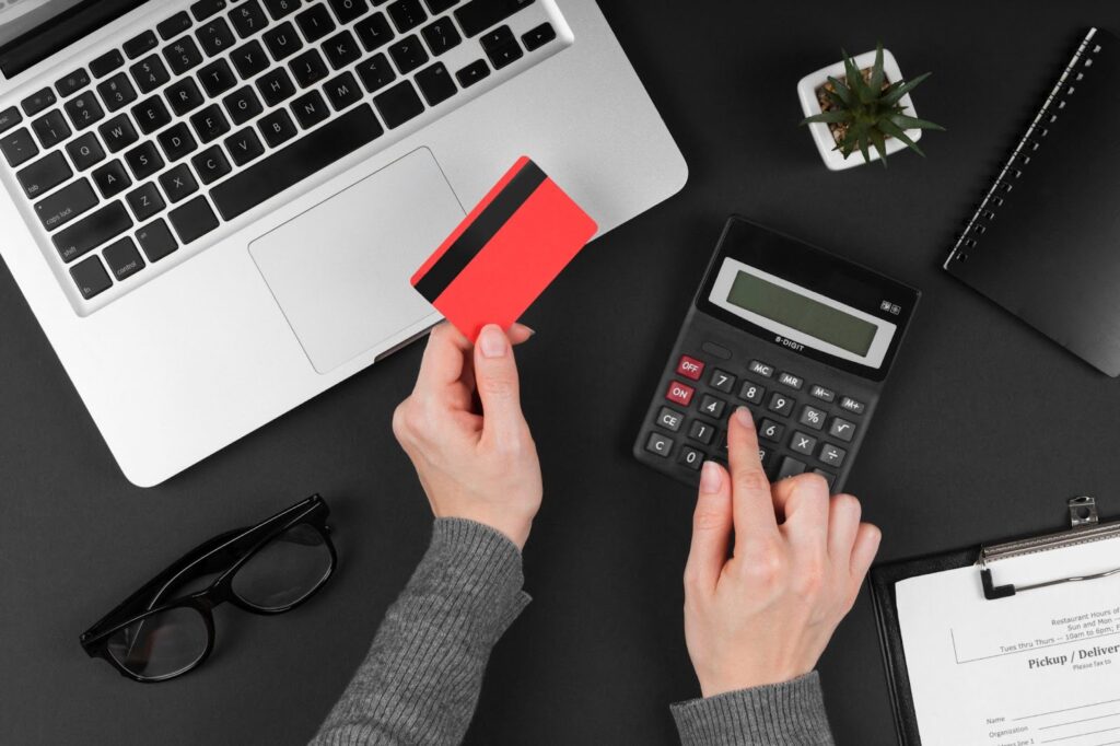 Top view of woman counting on a calculator holding a credit card in her hands