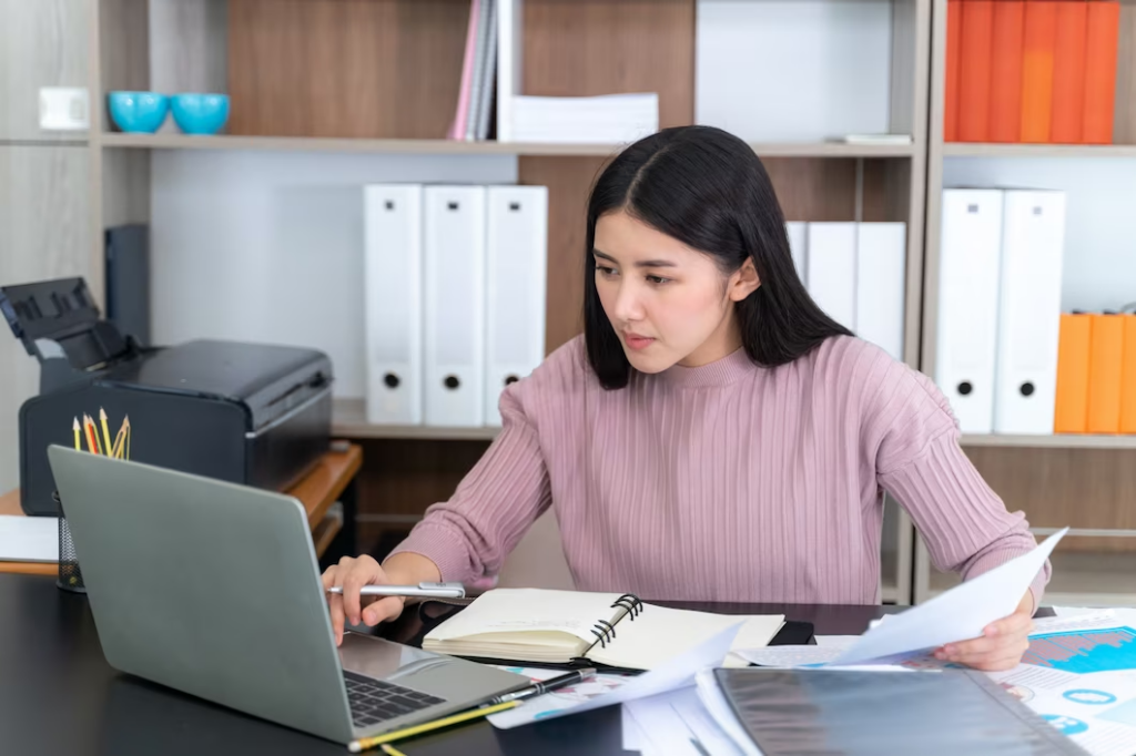 Image of a Woman working on laptop with documents